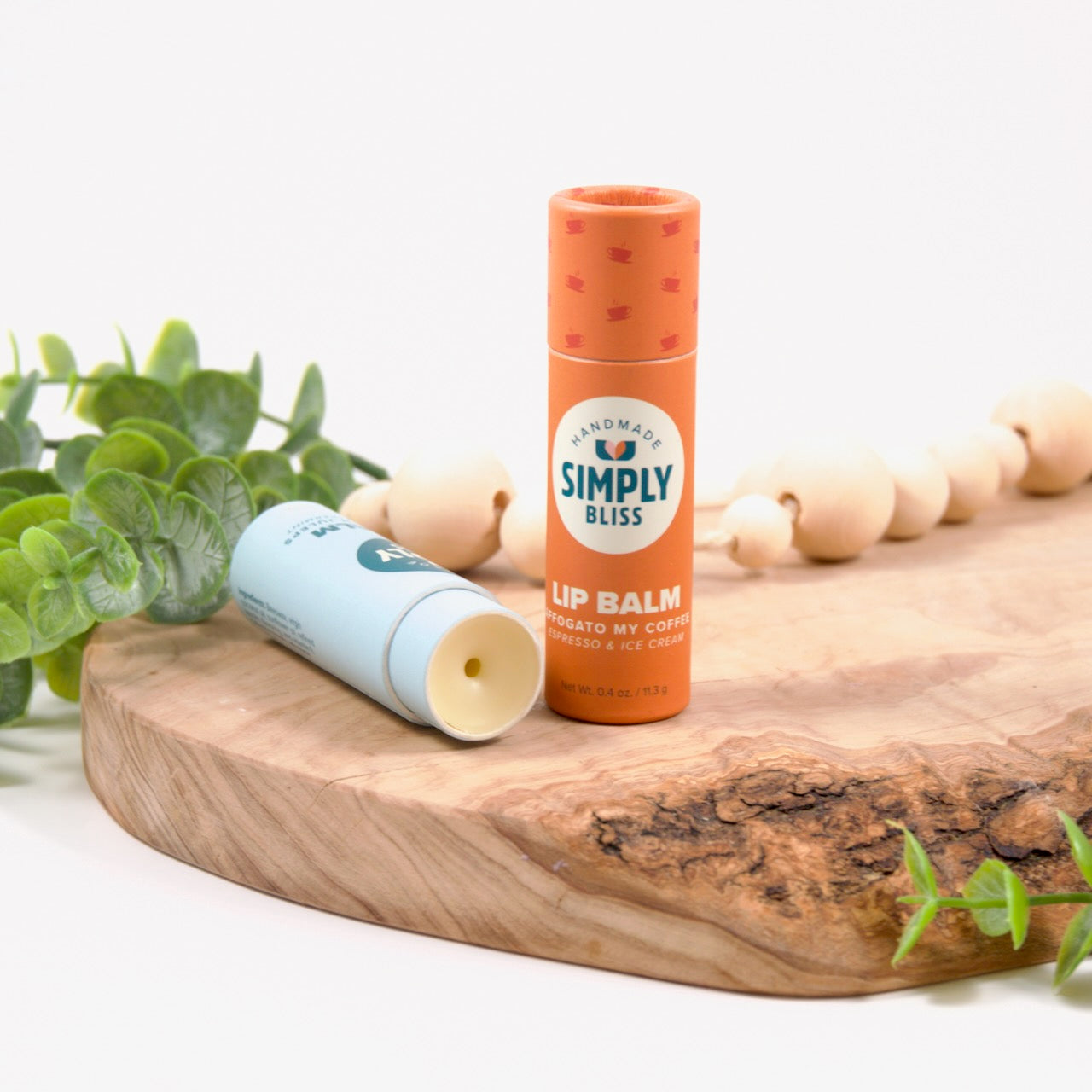 2 tubes of lip balm setting on a cutting board. One tube is laying on it's side open showing a creamy colored lip balm.